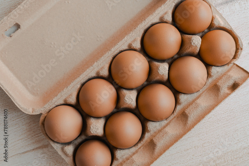 Close-up view of a carton of fresh brown eggs on a wooden surface, representing organic farm produce.