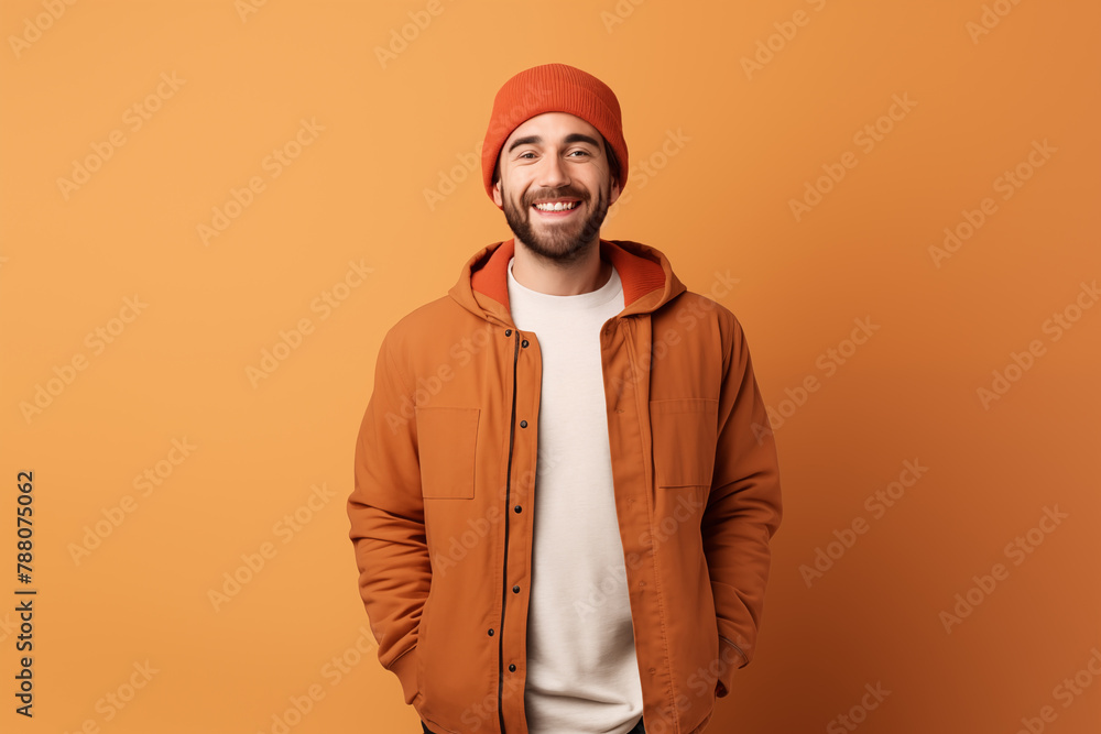 A beaming young man in a casual orange jacket and beanie exudes warmth and joy against a complementary orange background. A beaming young man in a casual orange jacket and beanie exudes warmth and joy against a complementary orange background.