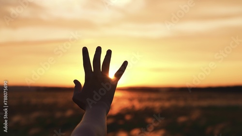 Woman stretched out hand sunset silhouette. Palm arm towards sun catching rays of evening morning dawn light in field meadow. Girl dreamily wistfully reaches for yellow orange sunshine with fingers