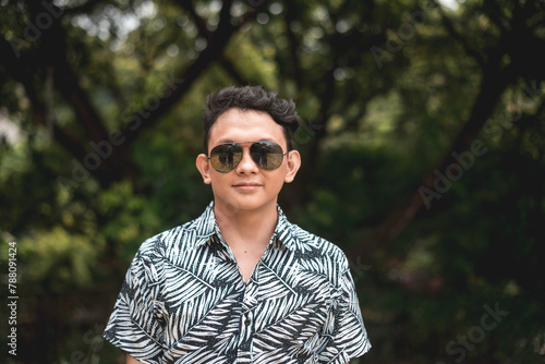 Summer vibes: Young man in colorful shirt posing with sunglasses against a forest backdrop