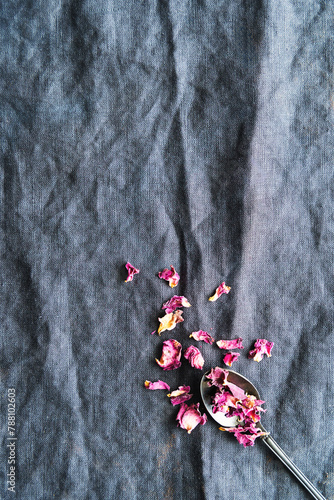 Getrocknete Rosenblätter auf einem Löffel. Blaues Leinen Tischtuch, Draufsicht.
