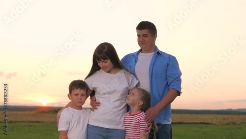 Happy family hugging posing together at sunset field sky nature landscape closeup. Mother father daughter and son affectionate cuddle embrace with love and tenderness unity bonding at meadow scenery © SUPER FOX