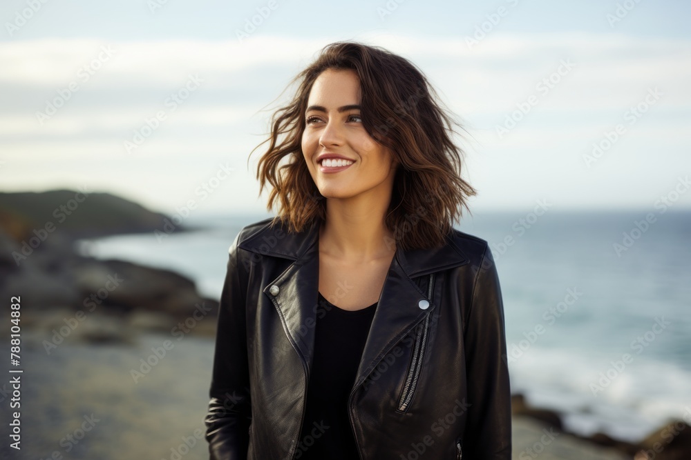 Portrait of a blissful woman in her 30s sporting a stylish leather blazer in front of serene seaside background
