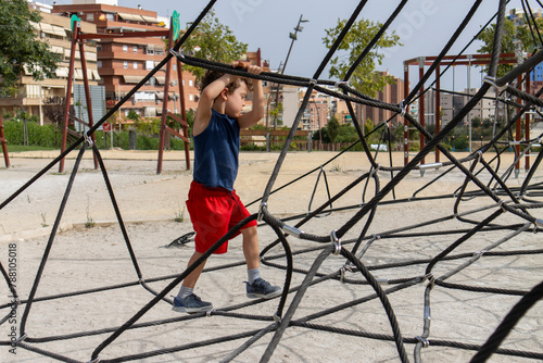 Child concentrating on crossing a complex rope structure at park.