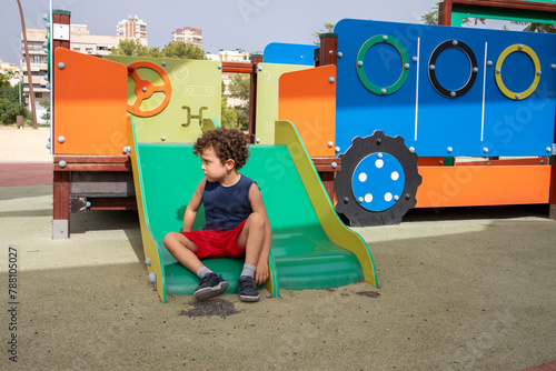Young Boy Sitting Alone on Playground Slide