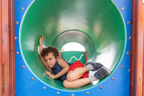 Curly-Haired Boy Playing in a Tunnel Slide