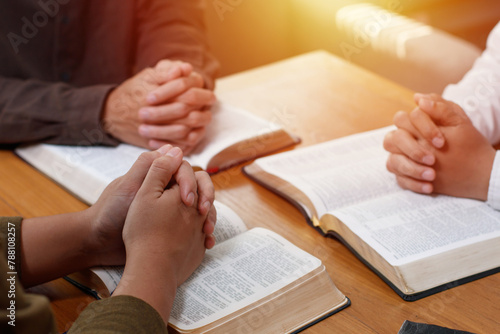 Power of hope or love, christian devotion background, bible study group concept. A group of people are gathered around a table with their hands outstretched in prayer over a Holy Bible. photo