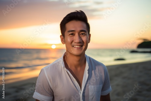 Portrait of a smiling asian man in his 30s wearing a sporty polo shirt isolated on stunning sunset beach background