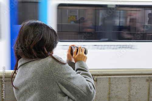 駅のプラットホームから電車を撮影する女性
