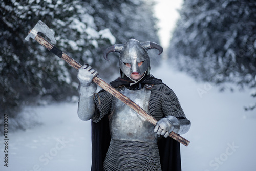 Portrait of a medieval fantasy warrior in a horned helmet, steel cuirass, chain mail with a two-handed ax in his hands, standing in a fighting position against the backdrop of a winter forest.