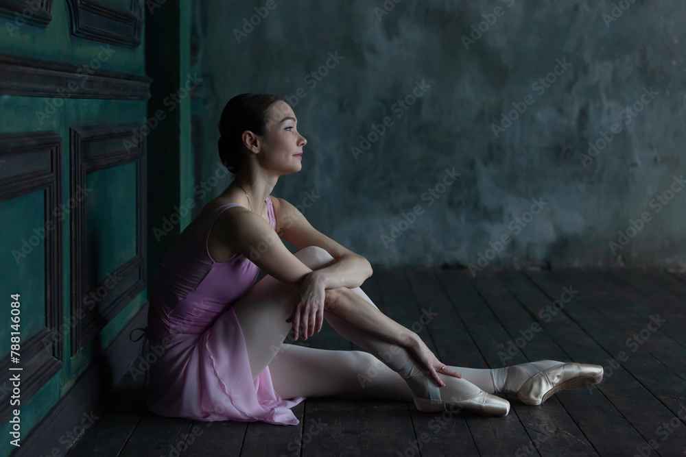Ballerina in pointe shoes sits on the floor.