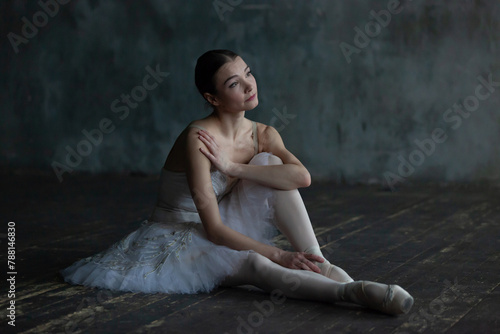 Portrait of a resting ballerina sitting on a wooden floor.
