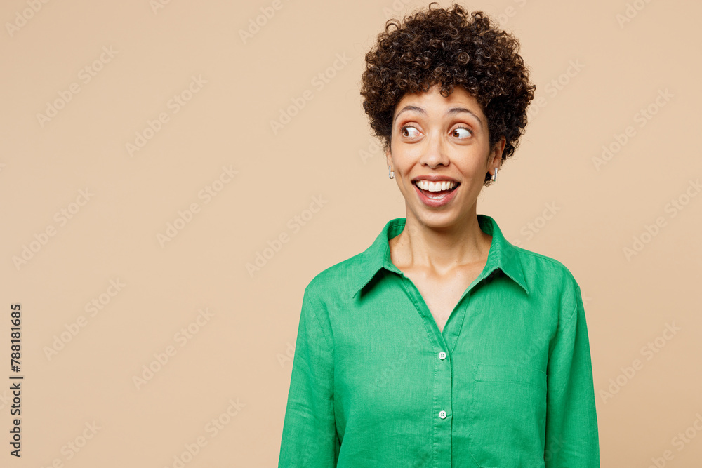 Young shocked surprised excited fun woman of African American ethnicity wears green shirt casual clothes look aside on area isolated on plain pastel light beige background studio. Lifestyle concept. Young shocked surprised excited fun woman of African American ethnicity wears green shirt casual clothes look aside on area isolated on plain pastel light beige background studio. Lifestyle concept.