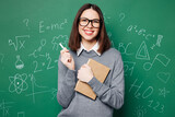 Young fun smart teacher woman wear grey casual shirt touch glasses hold in hand exercise book, pen isolated on green wall chalk blackboard background studio. Education in high school college concept.