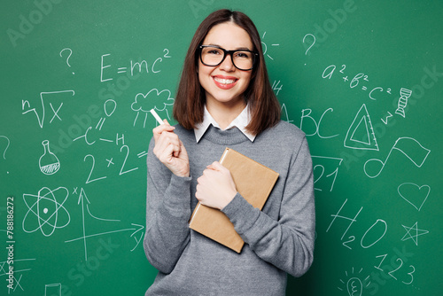 Young fun smart teacher woman wear grey casual shirt touch glasses hold in hand exercise book, pen isolated on green wall chalk blackboard background studio. Education in high school college concept. © ViDi Studio