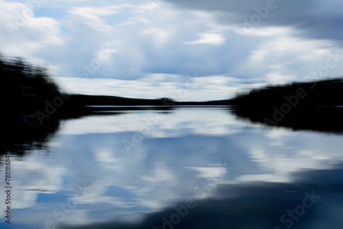 Intentional camera movement (ICM) image of a dream like lake scene with dark forest and cloudy spring sky reflectiong on water surface created by motion blur. photo