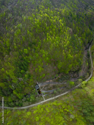 Aerial drone view above an overflowing small dam built on a mountain river. The concrete structure is located on a valley in Cozia Massif. Carpathia, Romania, Springtime. Trees are blooming