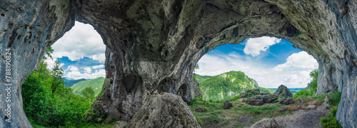 Viewpoint above mountains through a grotto, eroded in a calcareous cliff on a mountain. The tunnel has its walls covered with moss. The arches in the cave resemble the shape of two eyes. Carpathia