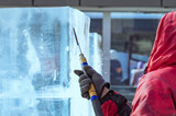 A sculptor processes a large ice cube with a sharp hand tool. Ice dust and ice fragments in the air. Ice sculpture festival.