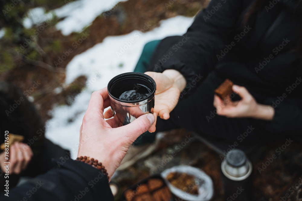 A man hands a woman a mug of tea on the background of the forest, camping in nature, people eating in the forest, treating a hot drink, a cup of coffee. A man hands a woman a mug of tea on the background of the forest, camping in nature, people eating in the forest, treating a hot drink, a cup of coffee.