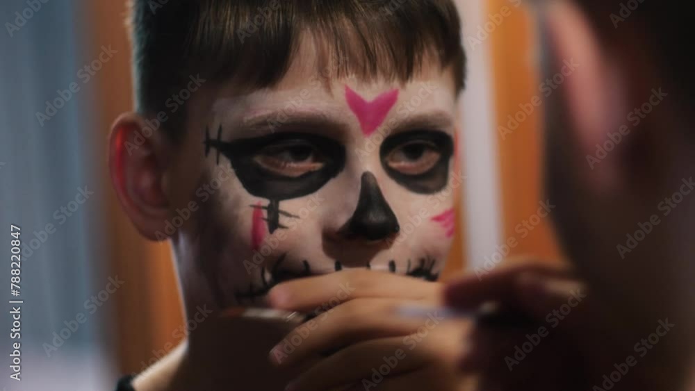 A Caucasian boy, 10 years old, looking in the mirror, paints his face in a mystical image with makeup for the holiday of Halloween or the Day of the Dead. A Caucasian boy, 10 years old, looking in the mirror, paints his face in a mystical image with makeup for the holiday of Halloween or the Day of the Dead.