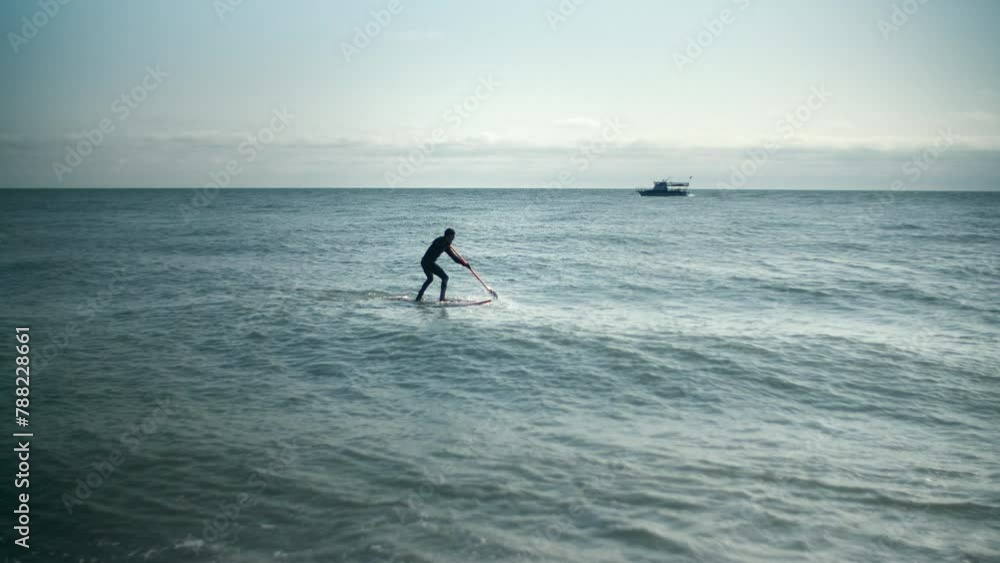 Man is floating on a surfboard, rowing with an oar. Male is doing paddleboarding or supboarding. Waves on the sea, surfing on the ocean. Hands pushing and pulling the paddle Man is floating on a surfboard, rowing with an oar. Male is doing paddleboarding or supboarding. Waves on the sea, surfing on the ocean. Hands pushing and pulling the paddle
