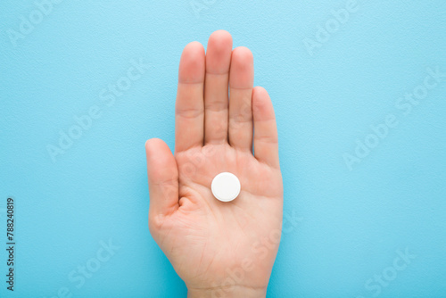 Young adult woman opened palm holding white pill of c vitamin on light blue table background. Pastel color. Receiving nutrition supplement. Closeup. Top down view.