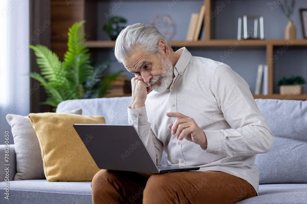 Senior man with beard using laptop on a comfortable sofa at home Senior man with beard using laptop on a comfortable sofa at home