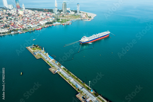Fuel tanker docked at port with cityscape backdrop, securing vital energy supply. © DedMityay