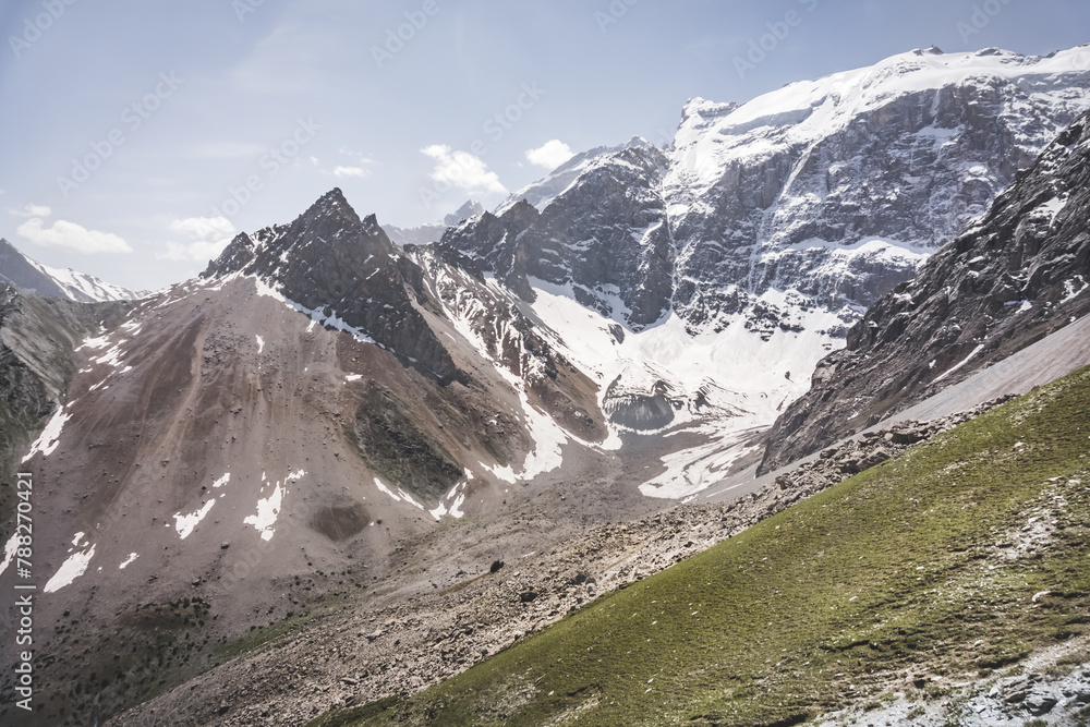 Panoramic landscape in the mountains with rocks and scree, with grass glades, snow and glaciers on a sunny summer day in the Fann Mountains in Tajikistan with mountain ranges