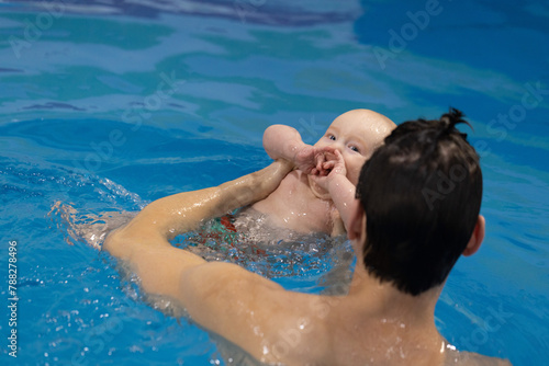 Smiling baby popping his knuckles and learn how to floating backstroke. Swimming lessons.