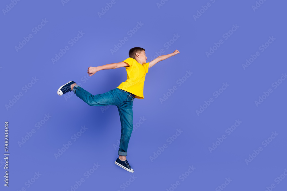 Full length photo of cheerful funny glad boy wear trendy yellow clothes fly air jump up empty space isolated on violet color background