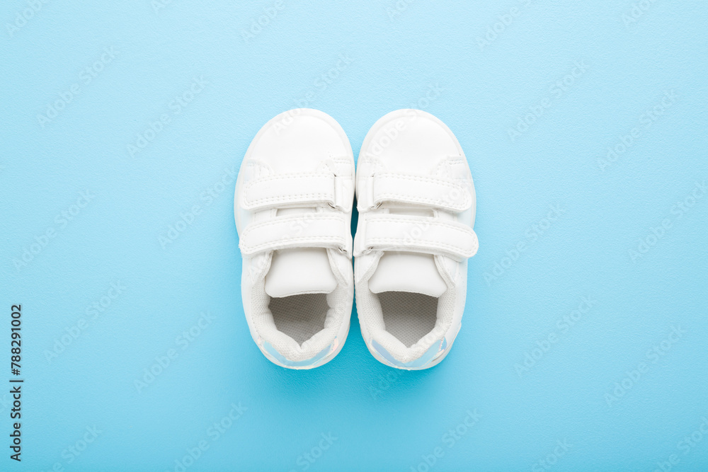New white leather sport shoes for little kid on light blue table background. Pastel color. Baby footwear. Closeup. Top down view. New white leather sport shoes for little kid on light blue table background. Pastel color. Baby footwear. Closeup. Top down view.
