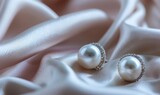 A set of pearl stud earrings arranged on a sleek satin material background