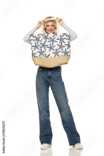 Beautiful young happy blonde woman in jeans with beach bag on white background