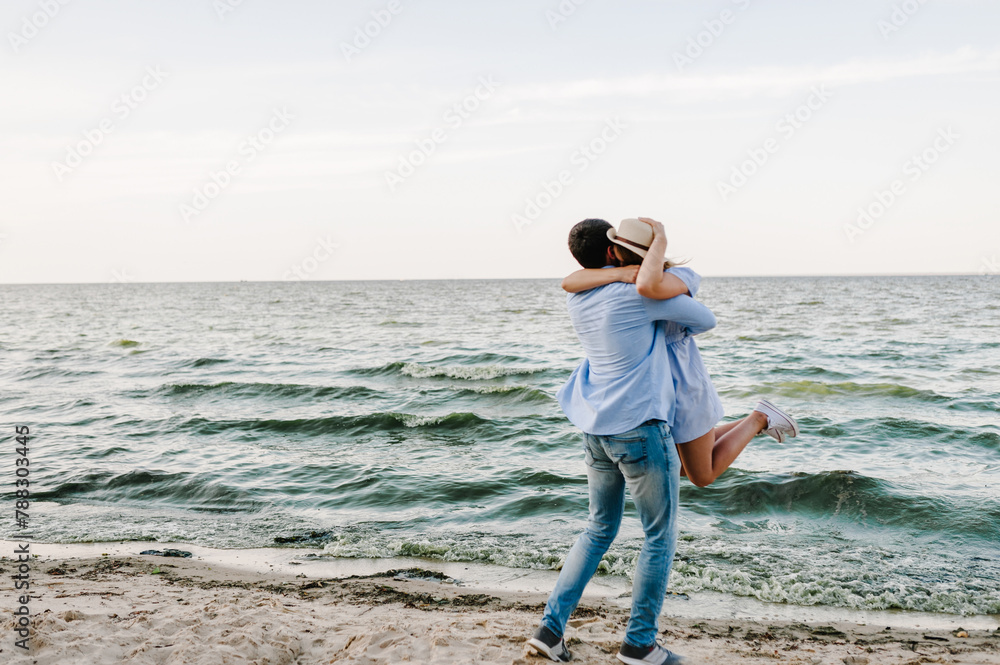 Female and male kisses on beach ocean and enjoying sunny summer day. Couple in love hugging and kissing each other on seashore. Man and woman standing on sand sea. Side view. Spending time together
