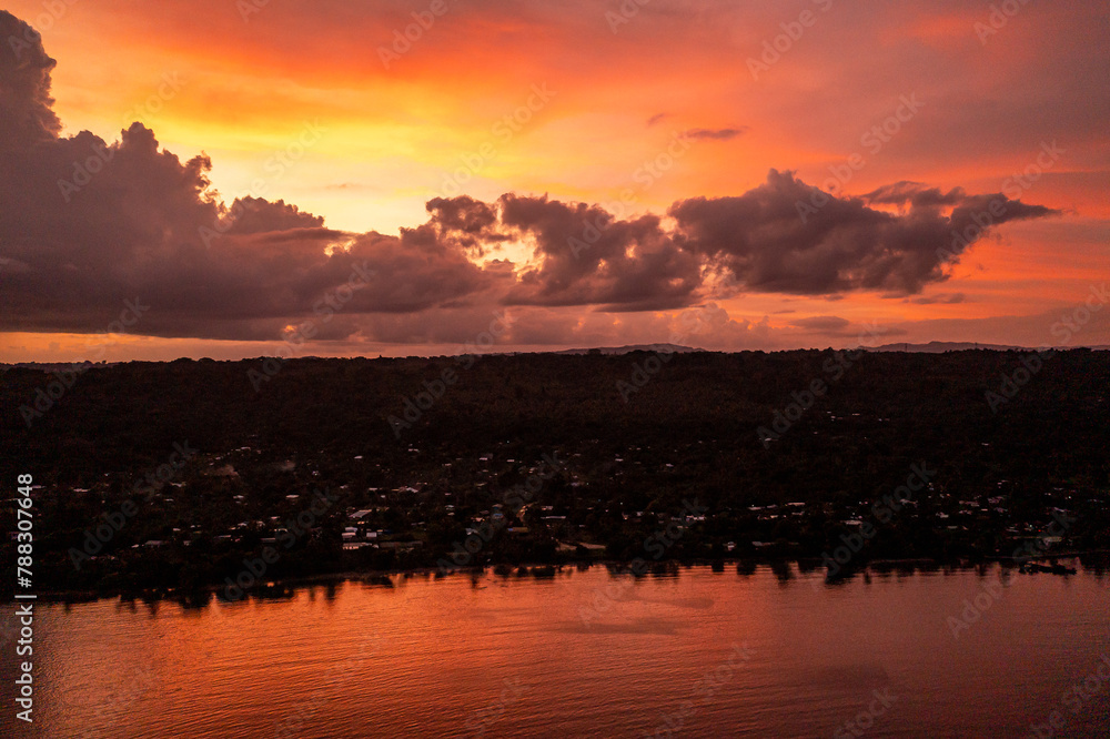 Fototapeta premium Scene of colorful sunset sky with clouds over evening city. Photo view from drone from the sea.