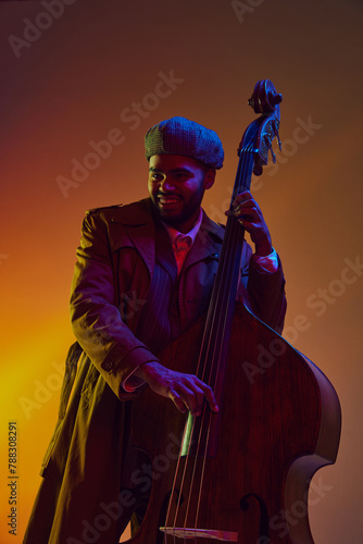 Bild auf Leinwand African-American man, musician in vintage coat and cap creates rhythm on bass in neon light against gradient background