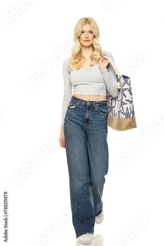 Beautiful young blonde woman in jeans with beach bag on white background