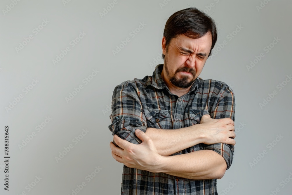 With a grimace, the man cautiously extended his arm, touching his painful elbow, his facial expression contorted with discomfort With a grimace, the man cautiously extended his arm, touching his painful elbow, his facial expression contorted with discomfort