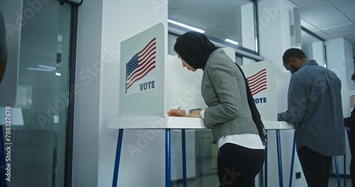 Muslim woman in hijab comes to vote in booth in polling station office. National Election Day in the United States. Political races of US presidential candidates. Concept of civic duty. Dolly shot.