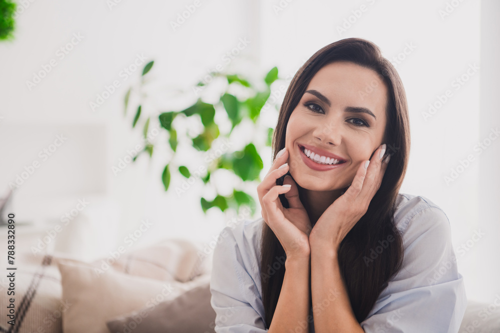 Photo of dreamy pretty lady dressed blue shirt smiling hands cheeks enjoying weekend indoors house room Photo of dreamy pretty lady dressed blue shirt smiling hands cheeks enjoying weekend indoors house room