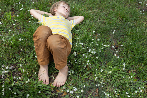 barefoot boy lies on the grass in the park. positive carefree childhood. Hello summer. relax, recharge with energy from nature. Earth Day