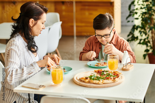 jolly mother eating pizza and drinking juice with her inclusive cute son with Down syndrome