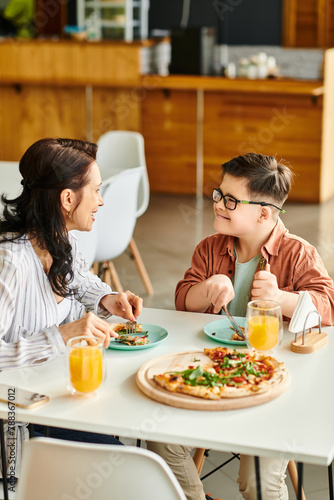 jolly mother eating pizza and drinking juice with her inclusive cute son with Down syndrome