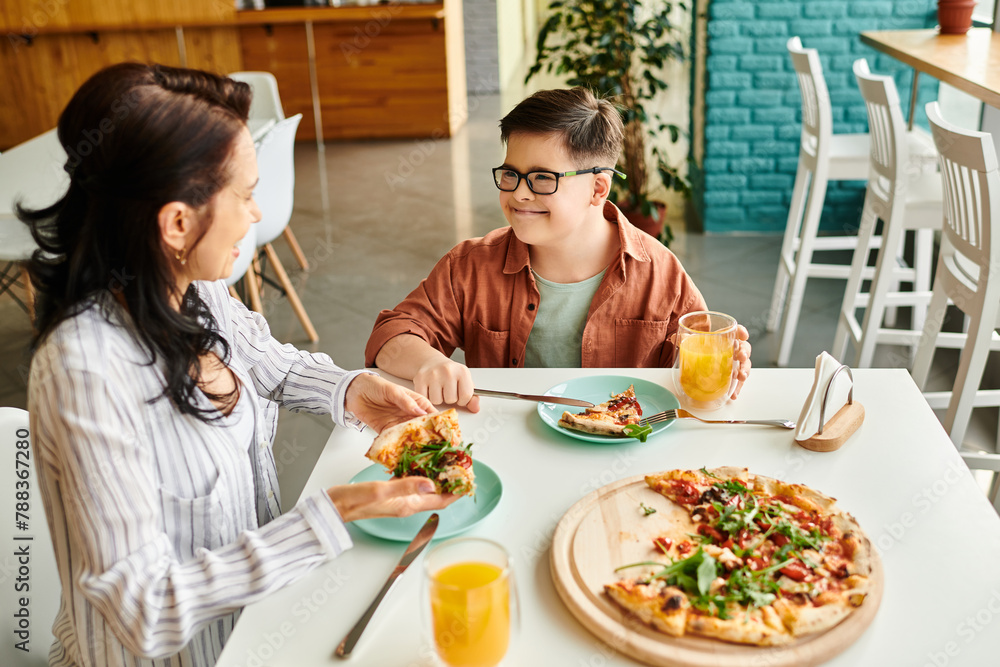 cheerful mother eating pizza and drinking juice with her inclusive cute son with Down syndrome cheerful mother eating pizza and drinking juice with her inclusive cute son with Down syndrome