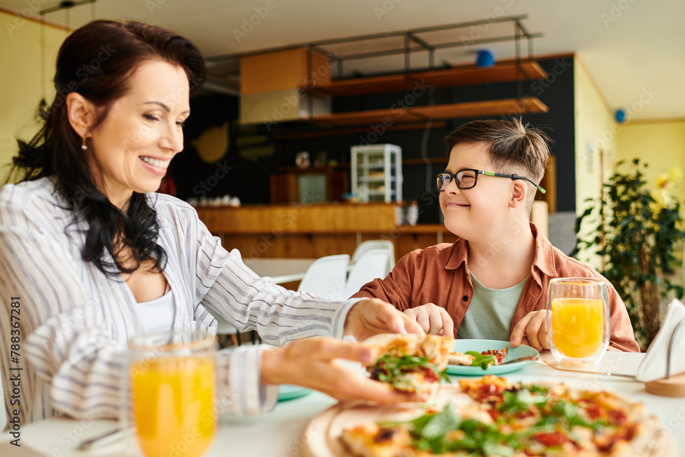 cheerful mother eating pizza and drinking juice with her inclusive cute son with Down syndrome cheerful mother eating pizza and drinking juice with her inclusive cute son with Down syndrome