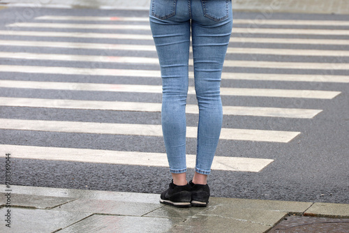 Female legs against the pedestrian crossing. Woman in jeans waiting the street at a crosswalk, road safety photo
