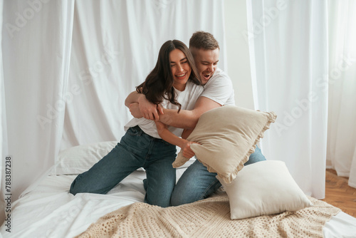 Soft pillows are in hands, playing. Young couple are together at home