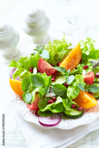 Salad with red and yellow Tomatoes and Pomegranate Seeds on bright wooden Background. Close up.